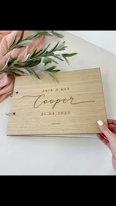 a wooden wedding guest book with greenery on the table next to it and a pink rose