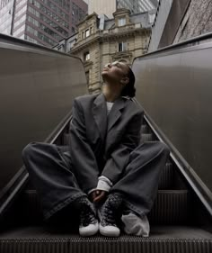 a woman is sitting on an escalator and looking up at the sky with her eyes closed