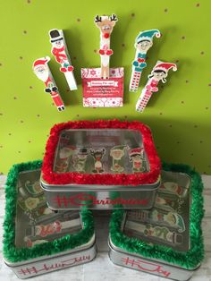 three tins with christmas decorations on them sitting in front of a green wall