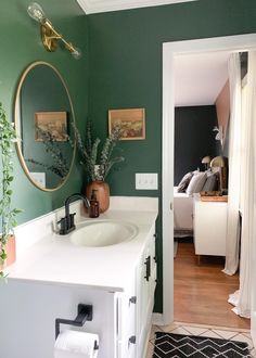 there is a bathroom with green walls and white counter tops, along with a gold framed mirror on the wall