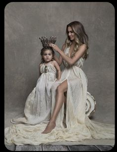 two women in white dresses sitting next to each other and one is holding a crown