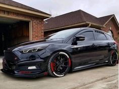 a black car is parked in front of a garage with red rims on it