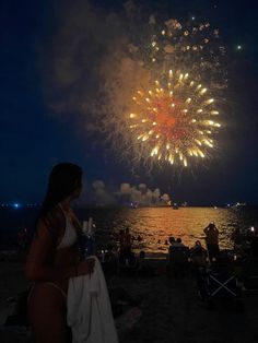 a woman standing on top of a sandy beach next to the ocean with fireworks in the sky