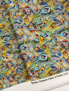 an image of colorful peacock feathers on a white tablecloth with the words endless treasures fabric of solito, inc