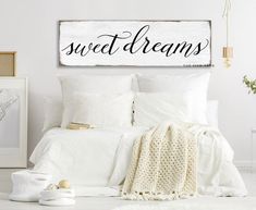 a bed with white sheets and pillows next to a wooden sign that says sweet dreams