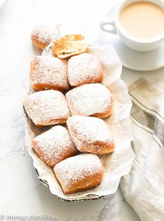 powdered sugar covered pastries on a plate next to a cup of coffee