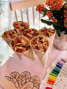 two cones filled with cereal and candy sitting on top of a table next to flowers