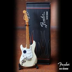 a white guitar sitting next to a box on top of a wooden table in front of a black background