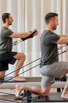 a man is doing exercises on a rowing machine while another man watches from the side