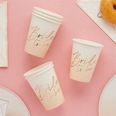 three paper cups with gold writing on them sitting next to a donut and napkins