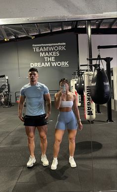 a man and woman standing next to each other in front of a gym equipment area