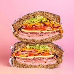 two halves of a sandwich with meat, lettuce and tomato on it against a pink background