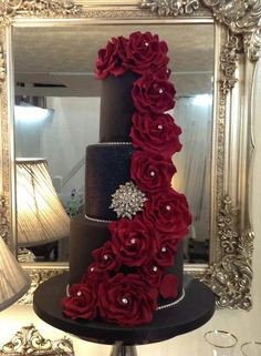 a three tiered wedding cake with red flowers on the top and black frosting