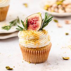 a cupcake with white frosting and topped with fresh figs, sprinkles and rosemary