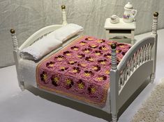 a crocheted blanket is on top of a small bed with white headboard and foot board