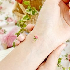 two hands holding each other with a small rose on the wrist and an apple basket in the background