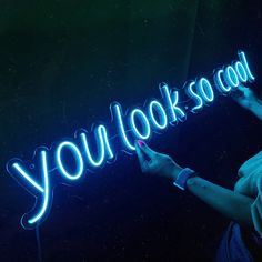 a woman standing in front of a neon sign that says you look so cool