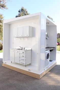 an outdoor kitchen is built into the side of a white building with cabinets and a washing machine in it