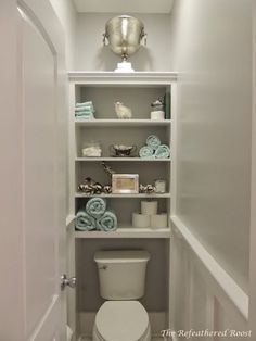 a white toilet sitting inside of a bathroom next to a shelf filled with blue towels