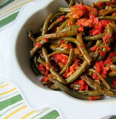 a white bowl filled with green beans covered in red sauce and topped with a spoon