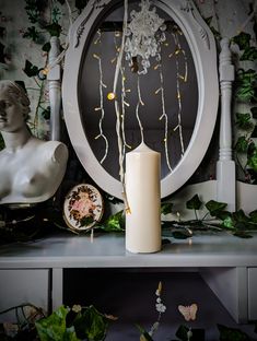 a white candle sitting on top of a table next to a statue and clock face