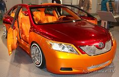 an orange and red car is parked in a showroom with people looking at it