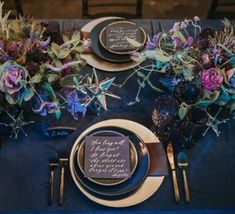 the table is set with plates, silverware and purple flowers