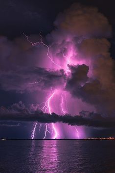 a lightning storm over the ocean on a cloudy night with bright purple lights and dark clouds