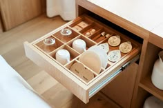 an open drawer on the side of a bed with dishes and cups in it,