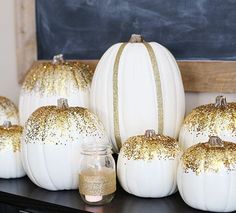 white pumpkins with gold glitter on them sitting in front of a chalkboard wall