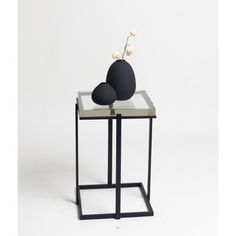 a black and white vase sitting on top of a small table next to a rock