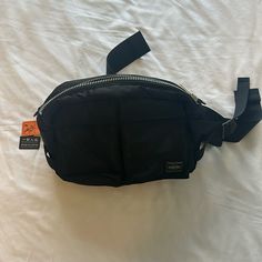 a black fanny bag sitting on top of a white sheet with an orange tag attached to it