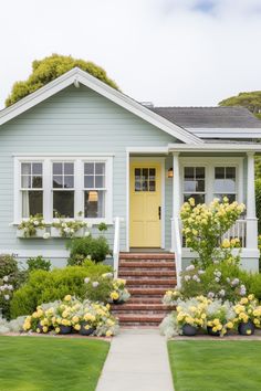 a blue house with yellow front door and steps leading up to the front door is surrounded by lush green grass