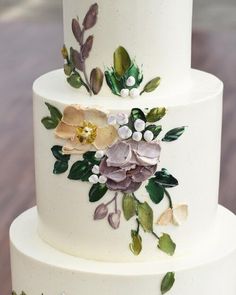 a three tiered white cake with flowers on the top and leaves on the bottom