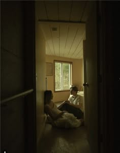 a man and woman sitting on the floor in a dark room looking at each other