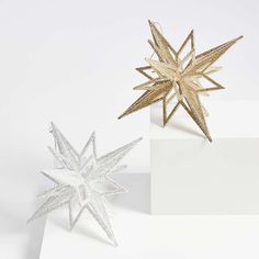 two gold and silver star decorations on top of a white box, one in the shape of a snowflake