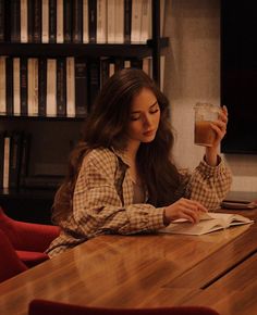 a woman sitting at a table with a book and drink in her hand while reading a book