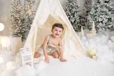 a little boy sitting in front of a teepee with christmas trees and presents around him