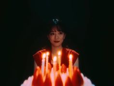 a woman sitting in front of a cake with lit candles