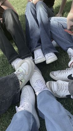 four people sitting on the grass with their feet crossed and one holding a cell phone