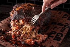 a person holding a fork and cutting into a roast beef on top of a paper wrapper