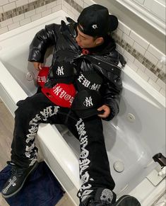 a young man sitting on top of a bath tub next to a white tiled wall