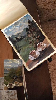 two coffee cups are sitting on a table with a landscape painted on the back of it