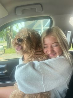 a woman sitting in the back seat of a car holding a dog