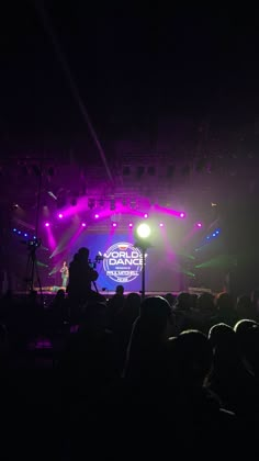 the stage is lit up with purple and green lights as people sit in front of it