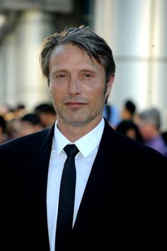 a man in a suit and tie posing for the camera with people behind him looking on