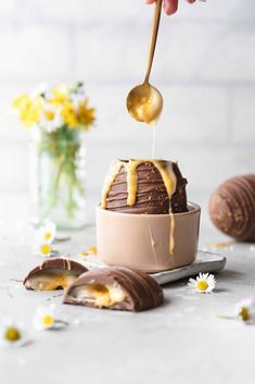 a person is spooning melted chocolate into a cake with flowers and daisies in the background