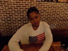 a woman sitting at a table in front of a brick wall with an american flag on it