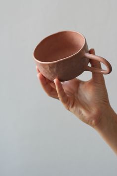 a hand holding a brown coffee cup in it's left hand, against a white background