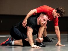 two men in red shirts and black shorts are wrestling